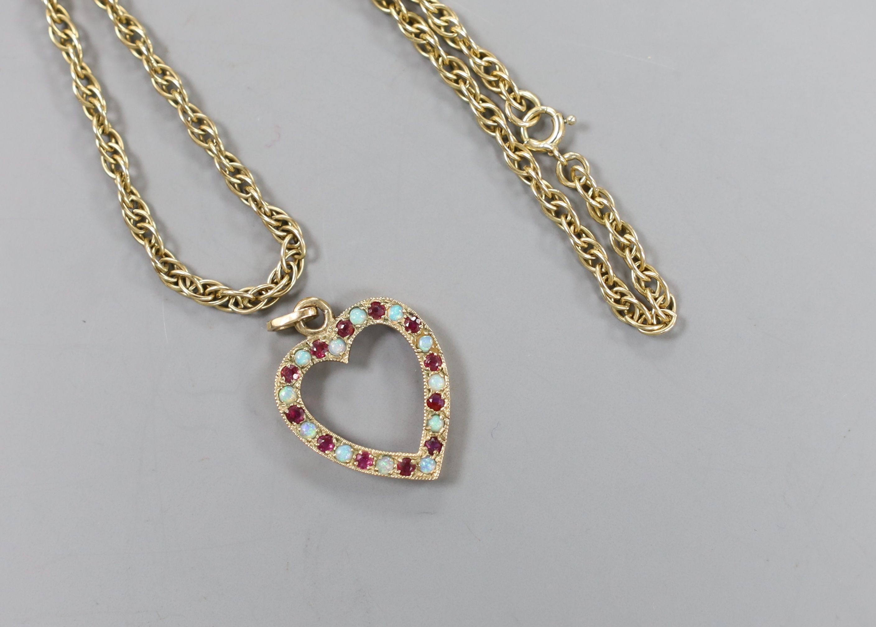 A modern 9ct gold, ruby and white opal set heart shaped open work pendant, 27mm and a 9ct gold chain, 38cm, gross weight 10.1 grams.